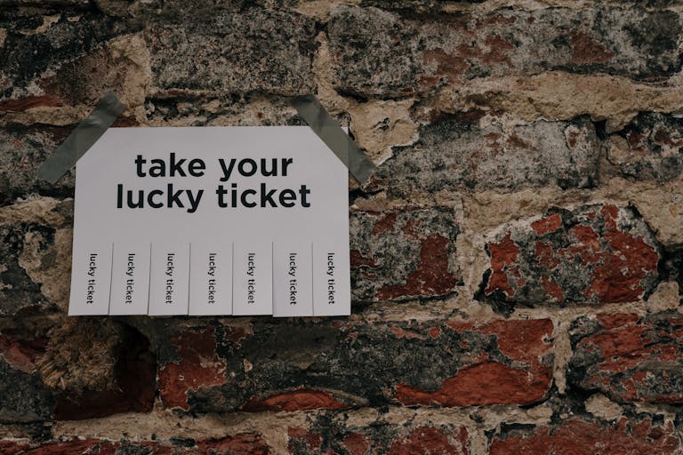 Close-up of a 'Take Your Lucky Ticket' sign taped to a rustic brick wall.