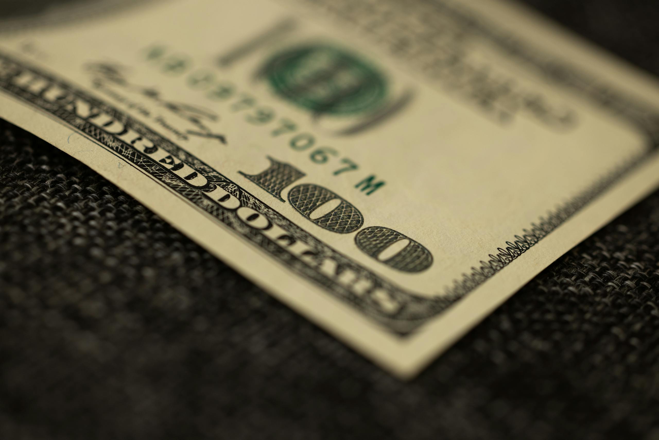 Detailed close-up of a hundred dollar bill resting on dark fabric surface, showcasing texture.